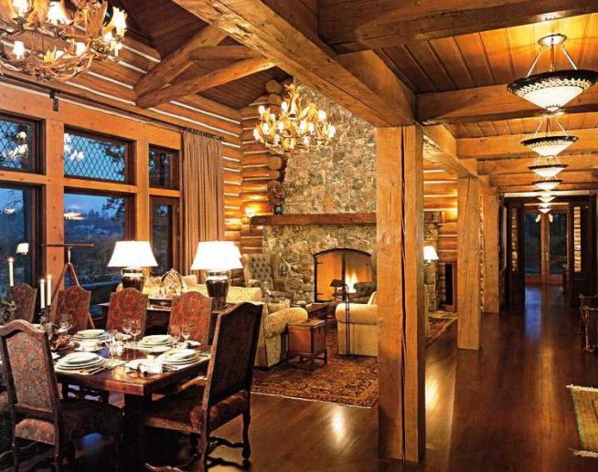 гостиная комната в бревенчатом доме с большим обеденным столом, крупными люстрами и камином с зажженным огнем
