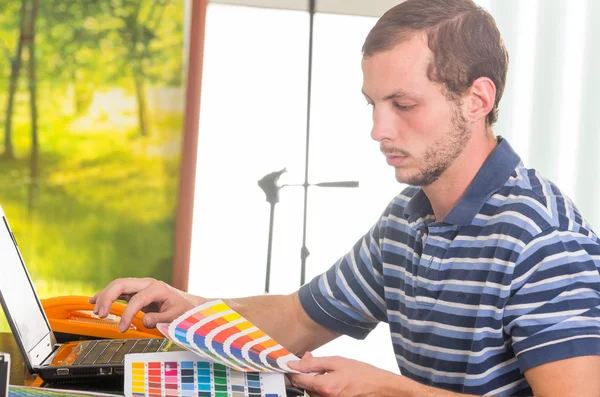 Человек носить синий белый полосатый футболку, сидя на рабочий стол с помощью телефона и глядя на пантона палитры, Colormap — стоковое фото