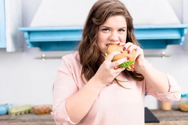 Портрет Молодой Женщины Избыточный Вес Ест Гамбургер Руках Кухне Дома — стоковое фото
