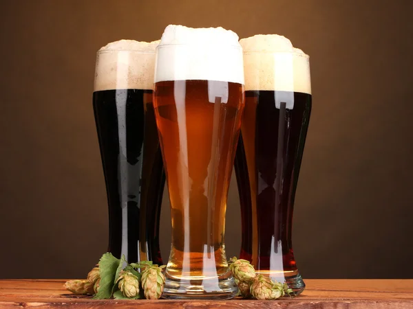Три очки с различных сортов пива и сесть на деревянный стол на коричневый фон — стоковое фото
